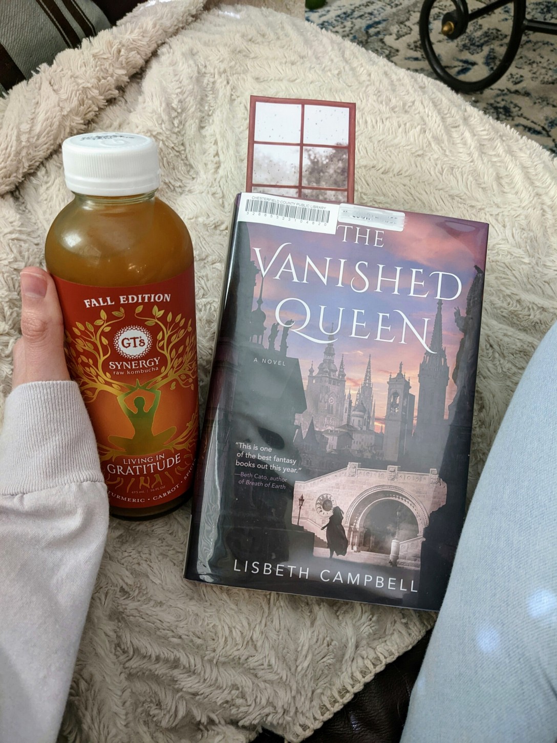 Alexis holds a fall kombucha bottle next to a library copy of The Vanished Queen.