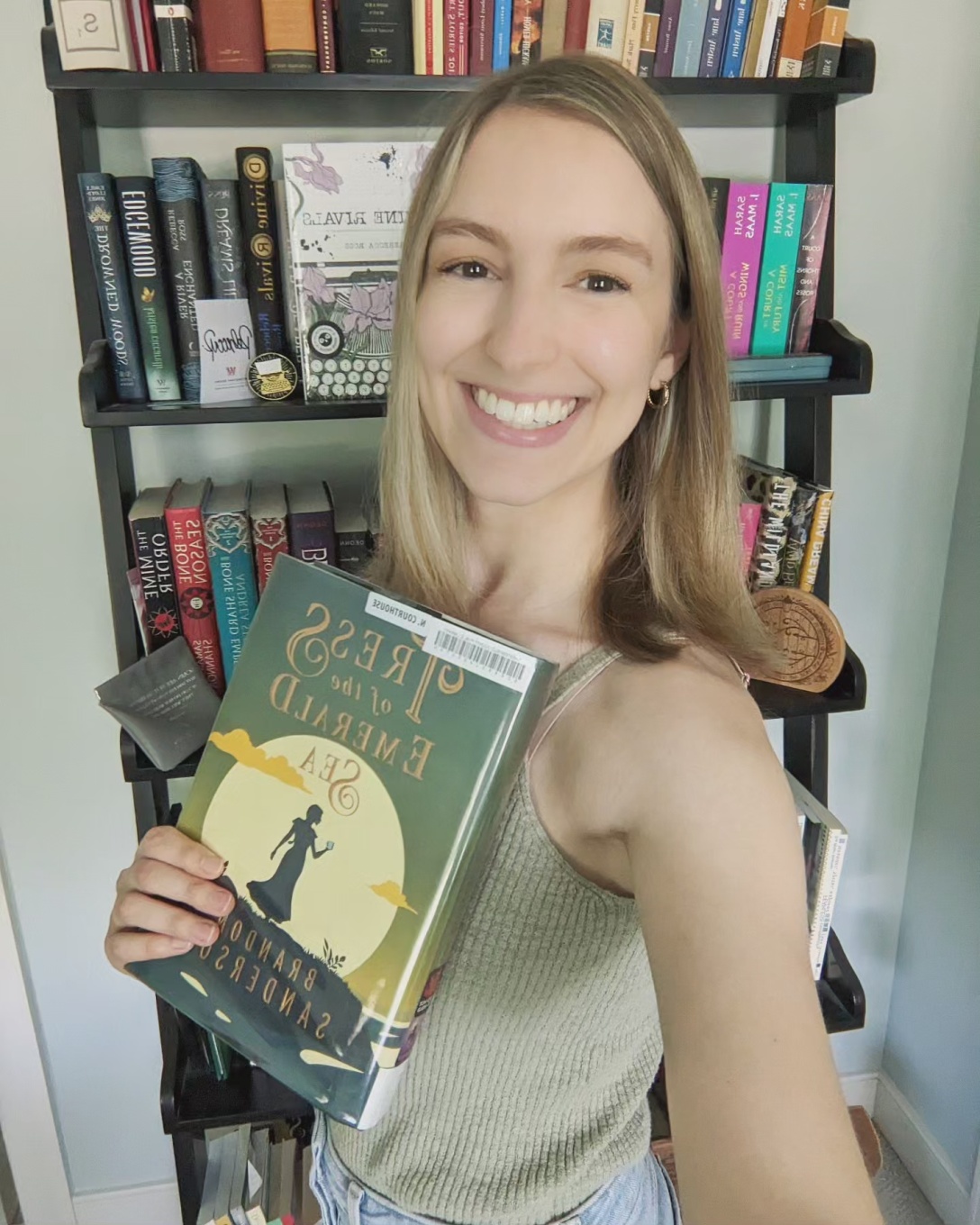 Alexis holds a library copy of the book in front of a bookshelf